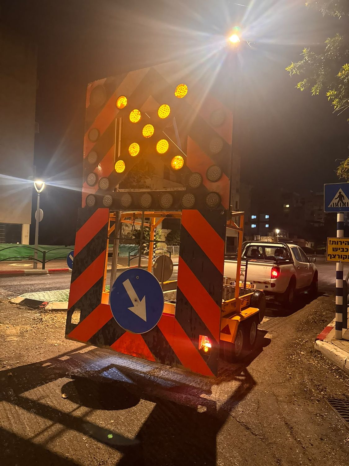 לוח חץ מואר בענבר בשעת לילה עם תמרור חובה כחול